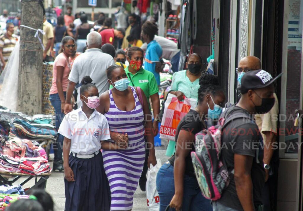 A woman holds the hand of a school child as they made their way through a crowded High Street San Fernando. - File photo/Marvin Hamilton