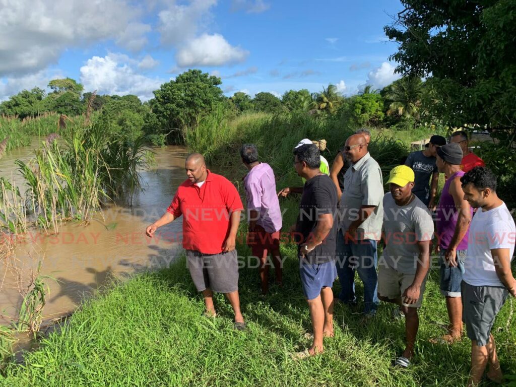 Residents of Ibis Gardens, Caroni gather on the Caroni river bank to show how much of it has fallen in on Friday.  Photo by Darren Bahaw