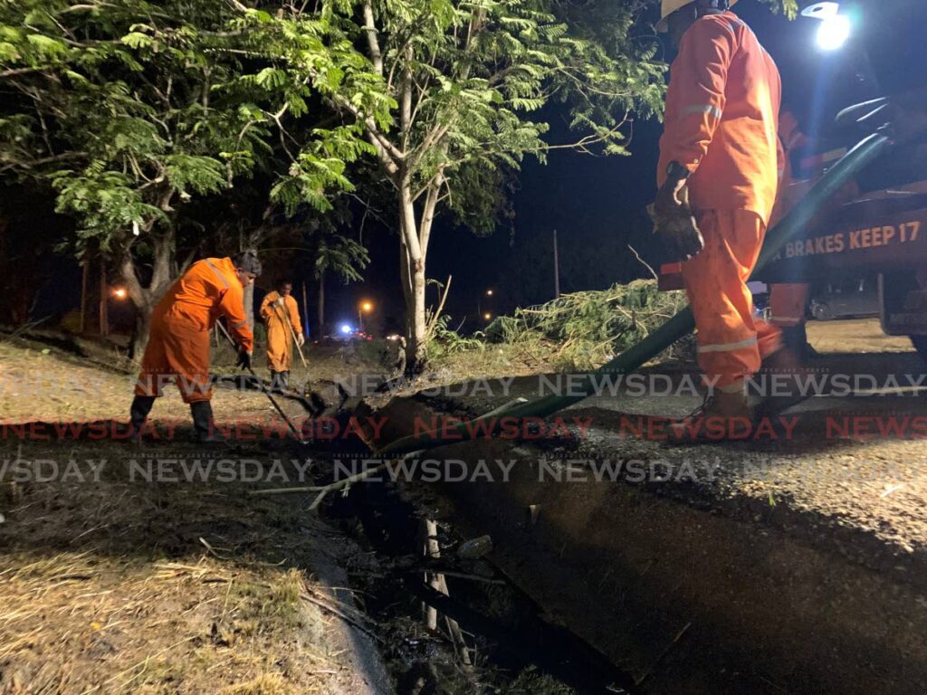 Workers remove a black oily substance which was dumped in a drain near the Caroni Bird Sanctuary on Thursday night.  - Photo by Darren Bahaw