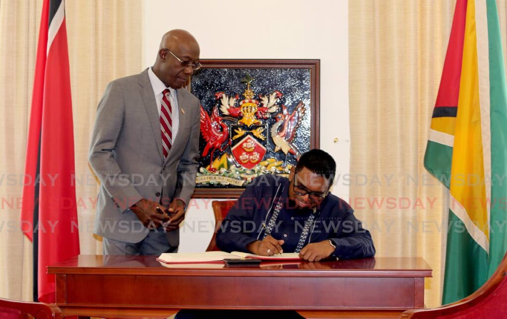 Prime Minister Dr Keith Rowley looks on as Guyana's President Dr Mohamed Irfaan Ali signs the visitors' book at the Diplomatic Centre, St Ann's on Thursday. Photo by Sureash Cholai