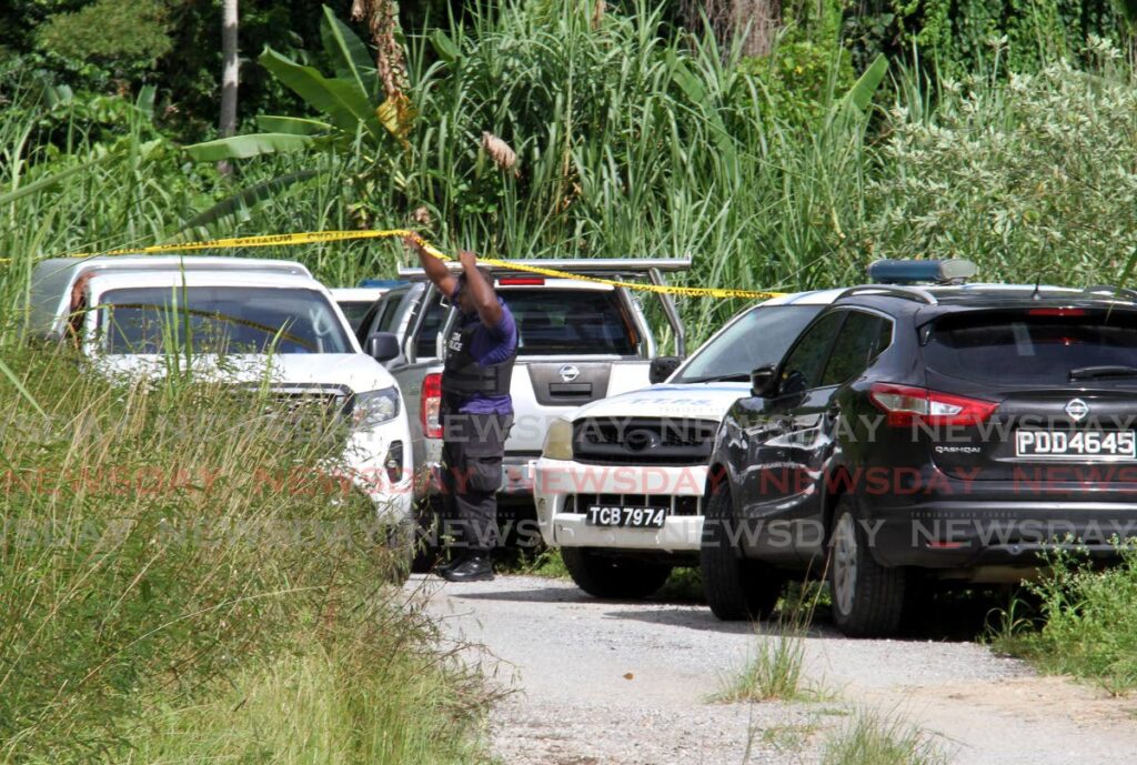 A Chaguaramas Development Authority estate constable raises the caution tape to allow undertakers to leave with the bodies of two unidentified men whose bodies were found at Guave Road, Chaguaramas on Friday. - AYANNA KINSALE