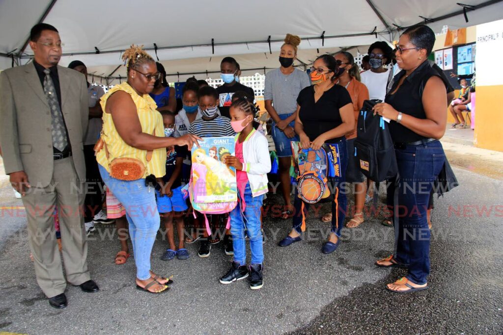 Pupils and parents of of children attending the St Dominic's RC Primary School, in backgroud, witness the donation of school supplies by Denise Grant, second from left, to a pupil on Saturday. At left is Sterling Jacob quality assurance and vicariate manager of the Roman Catholic School Board and school principal Nathalie Faria, right. - SUREASH CHOLAI