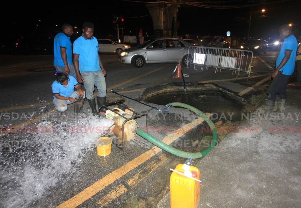 WASA employees pump out water from a ten-foot-wide sinkhole on the Western Main Road, St James, on Tuesday evening. - Angelo Marcelle