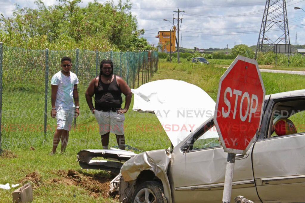 Tesfa Defour (right) and his passenger look on at his wrecked car which collided with a panel van at Tarouba on Sunday. Photo by Marvin Hamilton