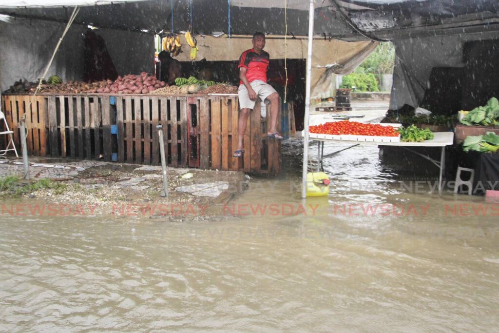 A man takes refuge under a vegetable stall along the SS Erin Road, Debe as heavy rains caused flooding on Monday. Photo by Lincoln Holder