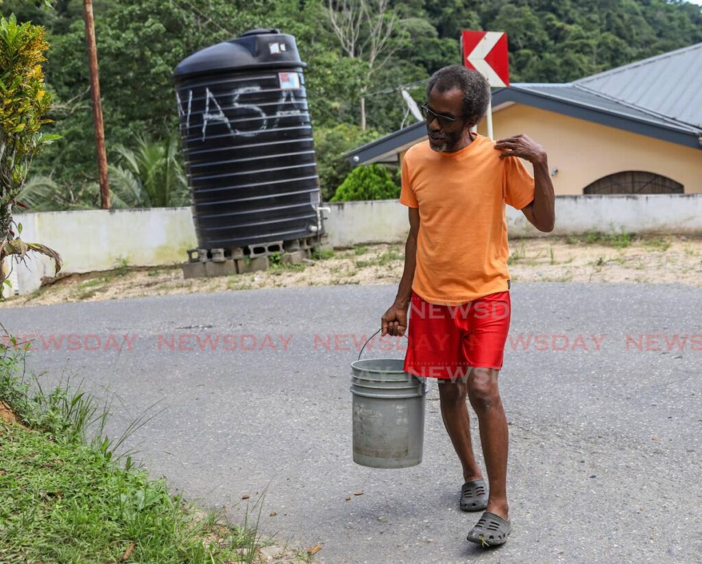 Winston Modeste carries a bucket of water he filled from a WASA tank in Lopinot on Saturday. - JEFF K MAYERS