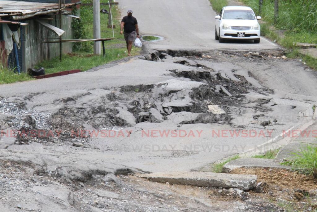 WHAT ROAD?: A man walks along the badly damaged Pluck Road in San Francique on Monday, while the driver of that car, too his time to consider the options available. PHOTO BY MARVIN HAMILTON   - 
