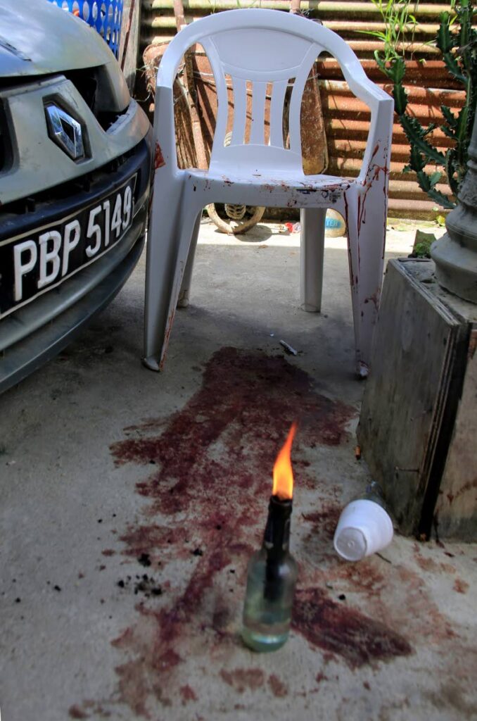 A lighted flambeau is placed on bloodstains in the yard of a house in Sangre Grande where seven people were shot and wounded while attending a wake on Wednesday night. PHOTO BY SUREASH CHOLAI - 