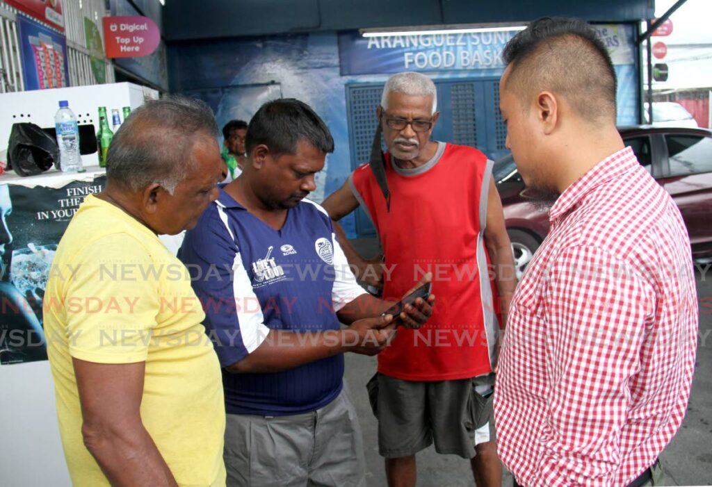 Aranguez residents look at a video of a man beating a caiman which died as Newsday reporter Shane Superville, right, interviewed them on Friday. The residents condemned the incident. Photo by Ayanna Kinsale 
