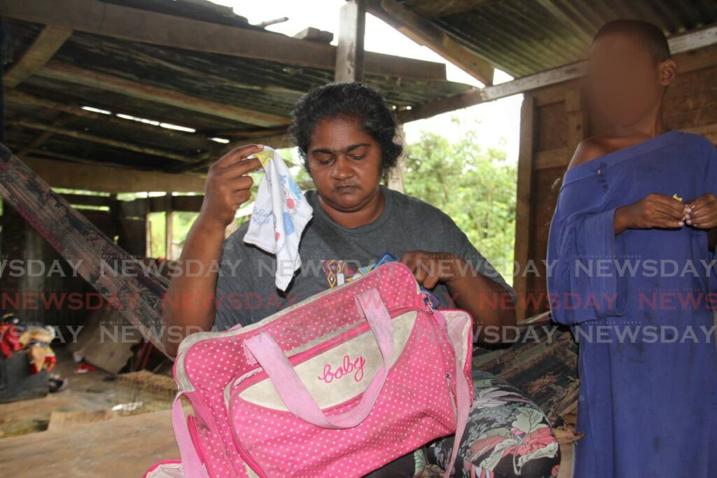 Sharmela Deonarine holds a baby bag and clothes at the place where nine-month-old Selieen Ramsaroop was force-fed a cocktail of milk, cereal and poison on Thursday. The baby died at hospital. File photo/Marvin Hamilton