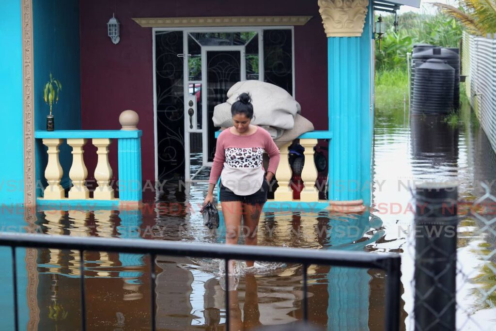A resident of Pluck Road, Woodland wades through her porch and yard after thundershowers triggered flooded in parts of south Trinidad on Thursday. - PHOTO BY ROGER JACOB