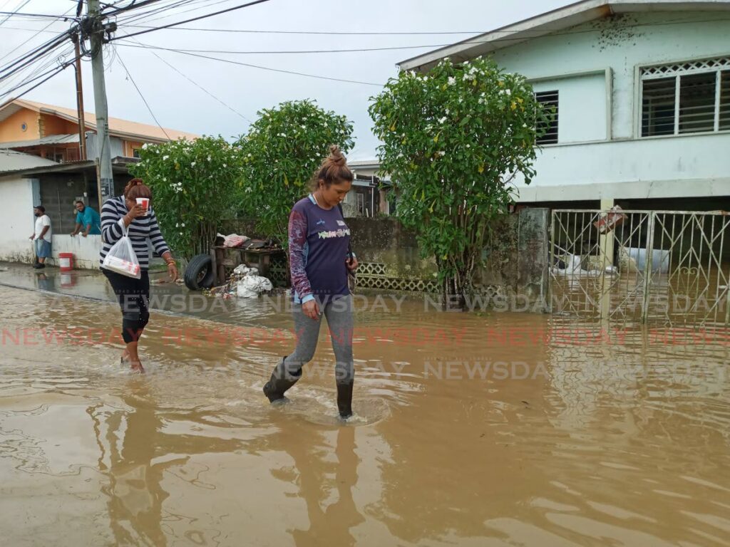 Women walk through flood water on Caroni South Bank Road in St Helena on Thursday. Several residents remain marooned. - Photo by Angelo Marcelle