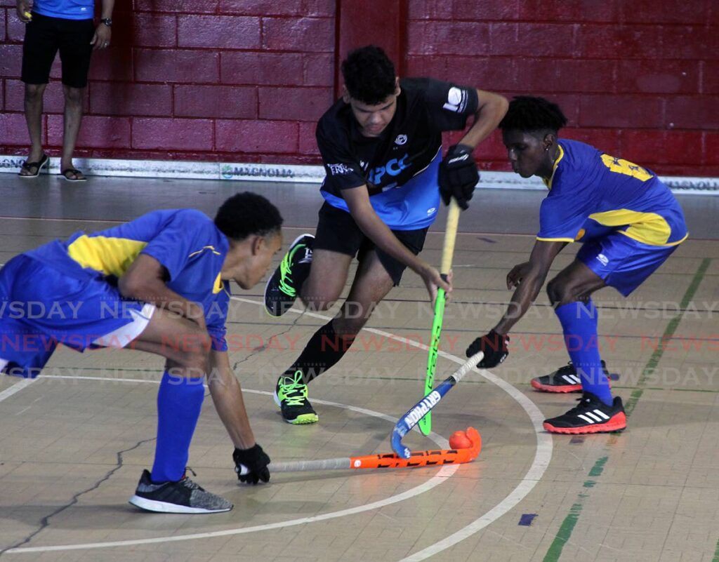 Alex Rowe of QPCC, tries to dribble pass two Fatima players, in their National Indoor hockey match, at the Woodbrook Youth Facility, Port of Spain on Sunday. Photo by Angelo Marcelle