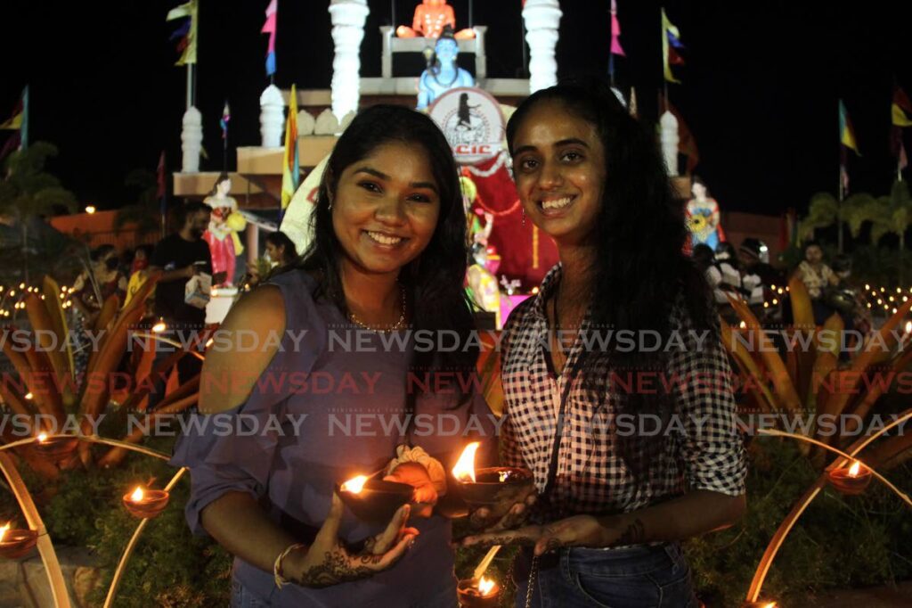 Friends Anjali Persad, left, and Sarah Jagoonanan share a moment while lighting deyas at the Divali Nagar in Chaguanas. - AYANNA KINSALE