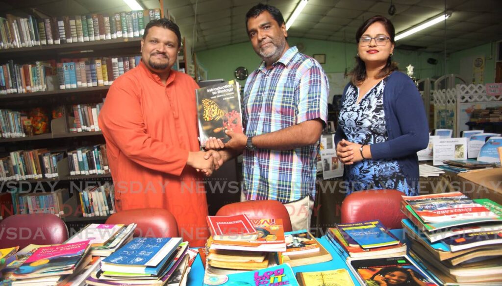 Pundit Keshava Gosine from the Sri Krsna Seva Ashram presents one of several hundred text books to principal of the Marabella North Secondary School, Sayeed Ali, while co-ordinator Ashti Gosine-Ramsumair looks on.  Photo by Lincoln Holder