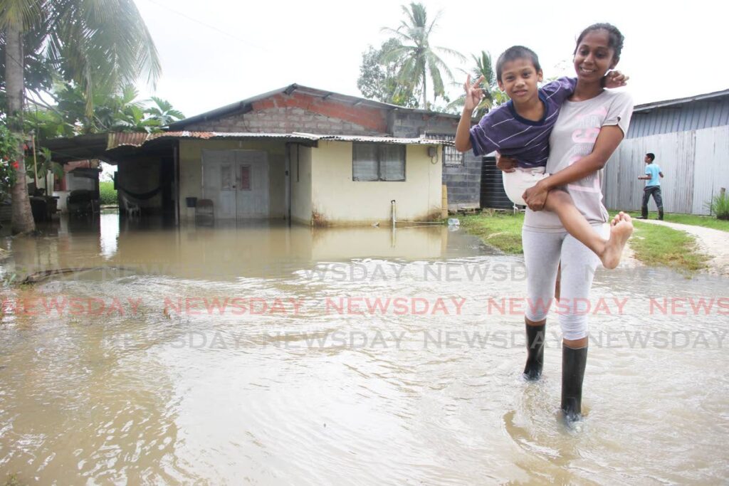 Angel Khan holds her son Aiden Bansgopaul, 6, as they walk through floodwaters near their home at Pluck Road, Woodland on Friday.  -Photo by Lincoln Holder