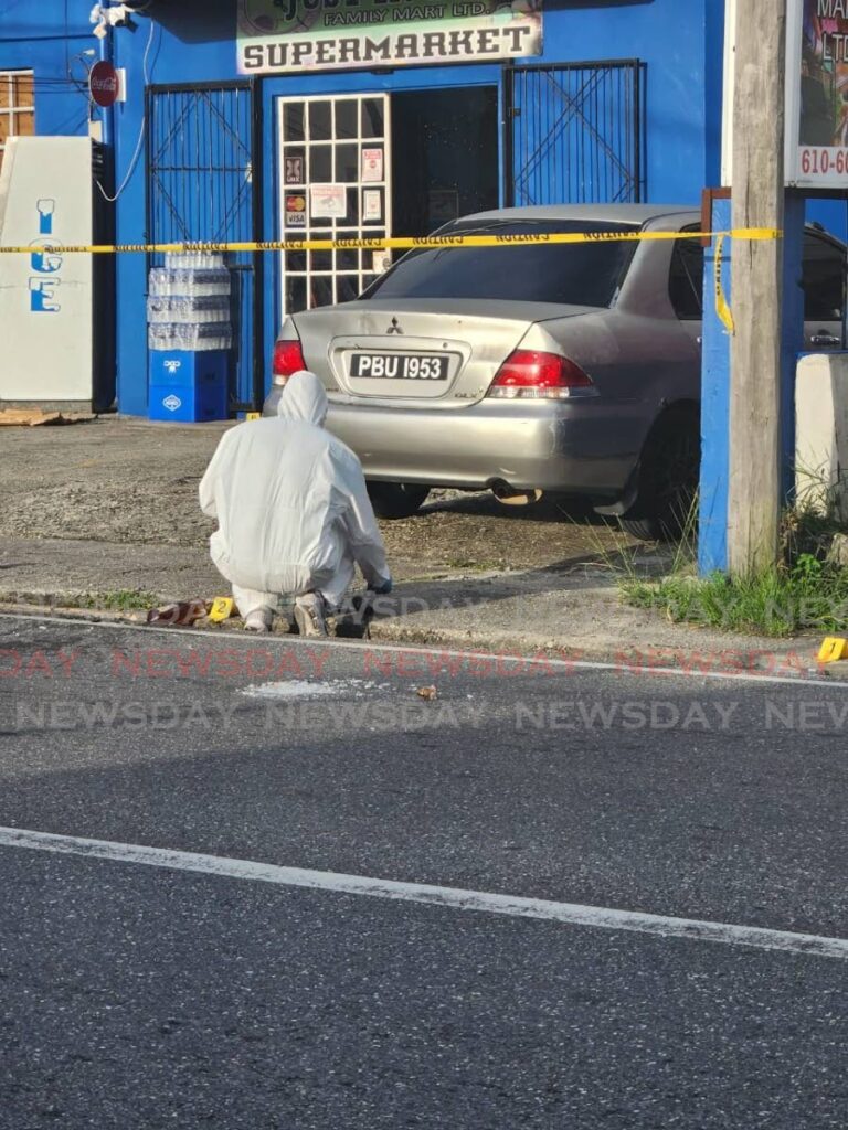 A crime scene unit officer gathers evidence outside Just in Time supermarket, on Cipero Street, San Fernando on Saturday where one bandit was killed during a robbery.  - Photo by Yvonne Webb