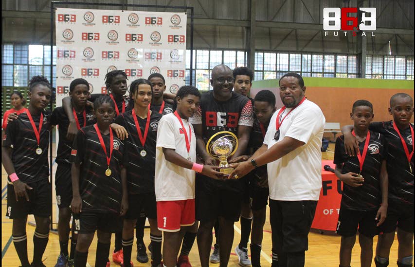 Members of Cox Football Academy being presented with the U14 Developmental Futsal Tournament Trophy - captain Mikhail Clement (centre), Geoffrey Edwards, president of the Futsal Association of Trinidad and Tobago (sixth from right) and coach Shurland Beckles (third from right). - 