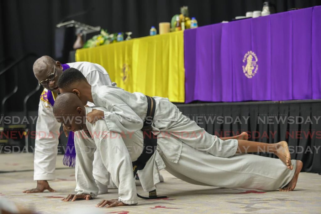 Andrew Roach does pushups with his son Adiah Roach on his back as  Professor Don Jacob founder and creator of the Purple Dragon Don Jitsu Ryu explains that the father has to work hard to support not only his son but his family as a whole, which demonstrates the importance of the man in the family during the 50th anniversary black belt grading, Hyatt Regency, Port of Spain on Saturday. - JEFF K MAYERS