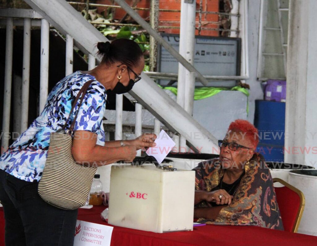 The presiding officer at the Pleasantville Secondary School, Pleasantville ensures the voter places her ballot in the box at the polling station for San Fernando East constituents during the PNM elections on Saturday. - AYANNA KINSALE