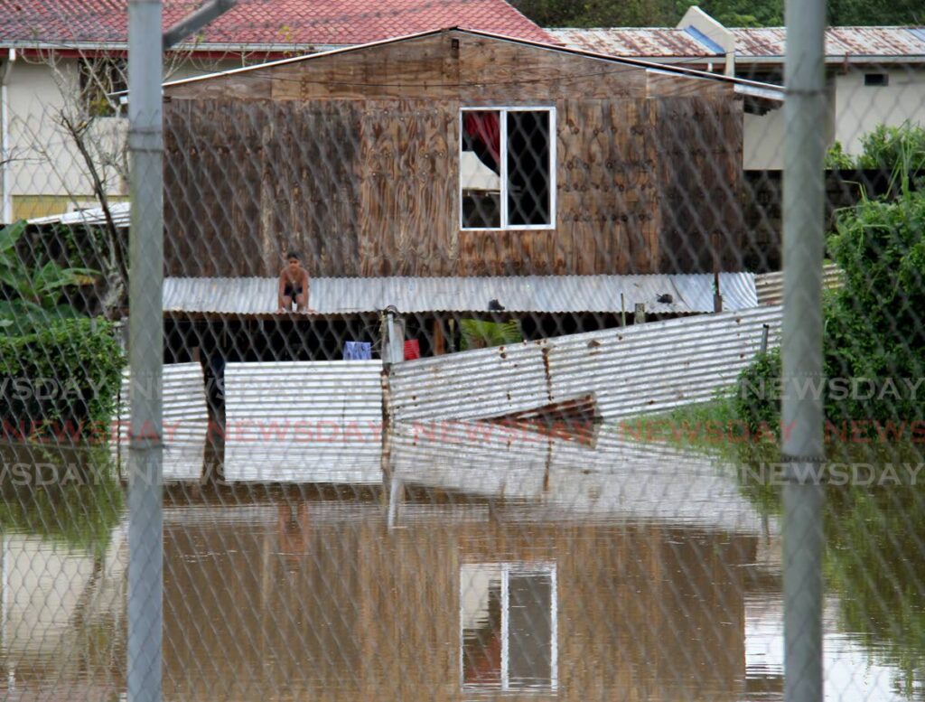 A boy is seen on a roof of a house surrounded by floodwater off Gasparillo Main Road, Gasparillo on Saturday. - Photo by Ayanna Kinsale