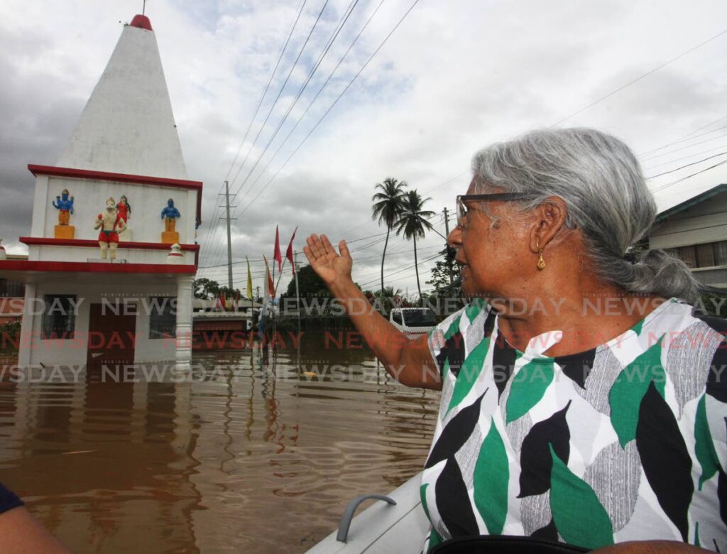I WILL RETURN: As she leaves in a dinghy, Gorlin Ramsingh devoutly gestures at the Hindu temple in the yard of her flooded-out Bamboo #2 home on Monday. Photo by Angelo Marcelle