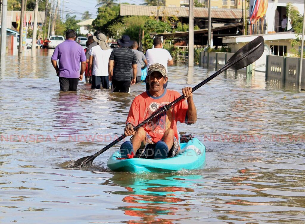 A resident of Jaffar Street, Bamboo No 2, Valsayn South, uses a canoe to navigate floodwaters in the area as other wade through the water on Tuesday. Photo by Roger Jacob