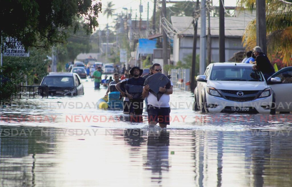 In this November 30 file photo, residents and volunteers wade through floodwaters with relief supplies and other items on Jaffar Street, Bamboo No 2, Valsayn South. Photo by Roger Jacob