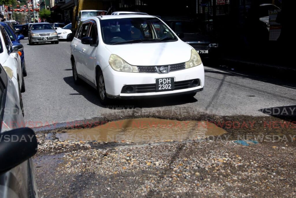 In this file photo, a motorist attempts to drive past this huge pothole on Queen Street in the heart of the city of Port of Spain.  - Photo by Sureash Cholai