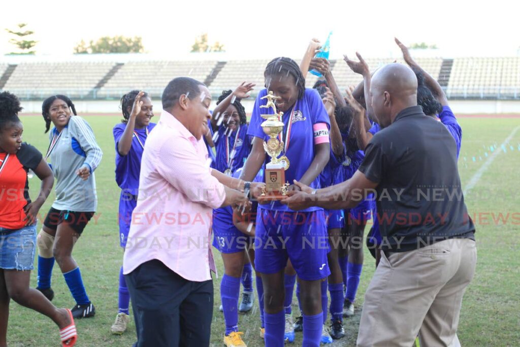 Five Rivers Secondary School captain Sharne Williams (C) is presented with the winner’s trophy by Secondary Schools Football League (SSFL) president  Merere Gonzales(L) after her team beat San Juan North Secondary in the SSFL Coca-Cola Girls Intercol East Zone final, at the Larry Gomes Stadium, Malabar, on Thursday. Five Rivers won 3-0.  Photo by Roger Jacob