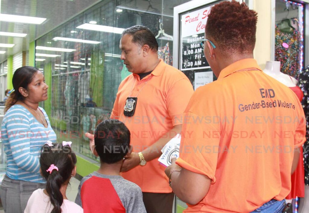 Special Victims Department's Insp Ramphal and Sgt Charles, speak with a woman with two childrent at Penal Junction about violence, particularly against women and children.  Photo by Marvin Hamilton