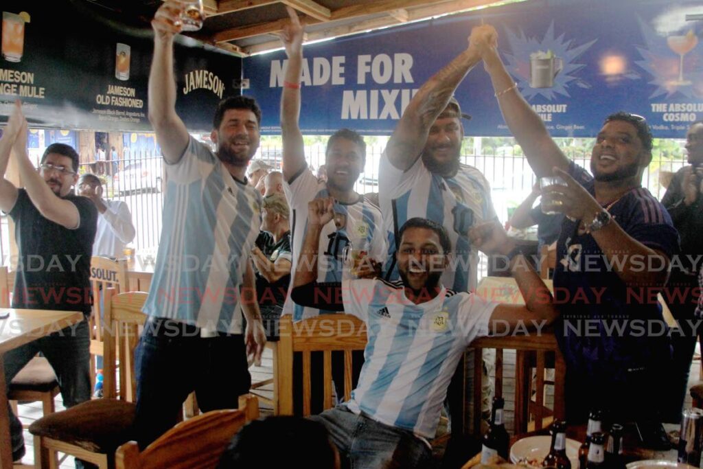 Patrons of CookKin Vibez in Woodbrook celebrate Argentina's victory over Croatia during the FIFA World Cup semi-final match on Tuesday. Andre Boodram, second from left, and Jeremie Palmer, second from right standing, were among those who were happy with the result. Photo by Roger Jacob