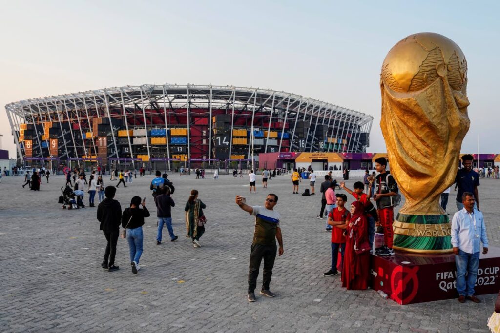 People pose for pictures next to a replica of the World Cup Trophy with the Stadium 974 in the background in Doha, Qatar. AP Photo - 