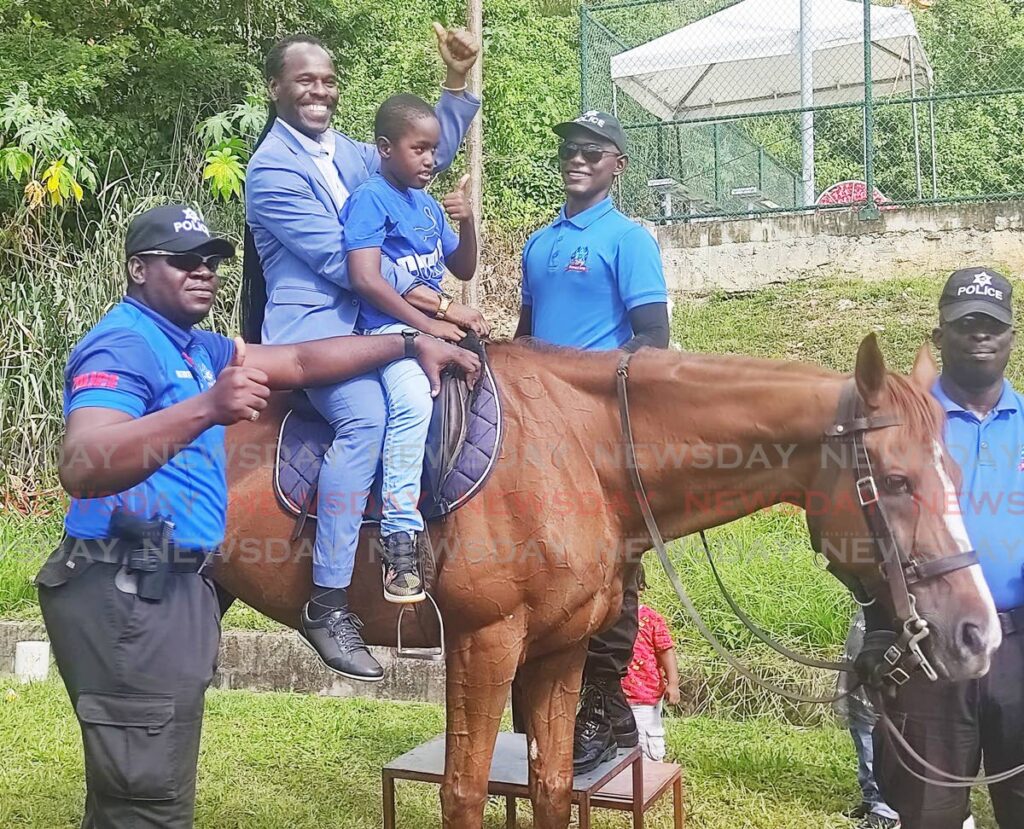 HORSING AROUND: National Security Minister Fitzgerald Hinds and Richard Roberts, nine, sit on police horse Ichabod  during the Christmas on the Hill Christmas treat for children in Laventille on Friday. Photo by Shane Superville