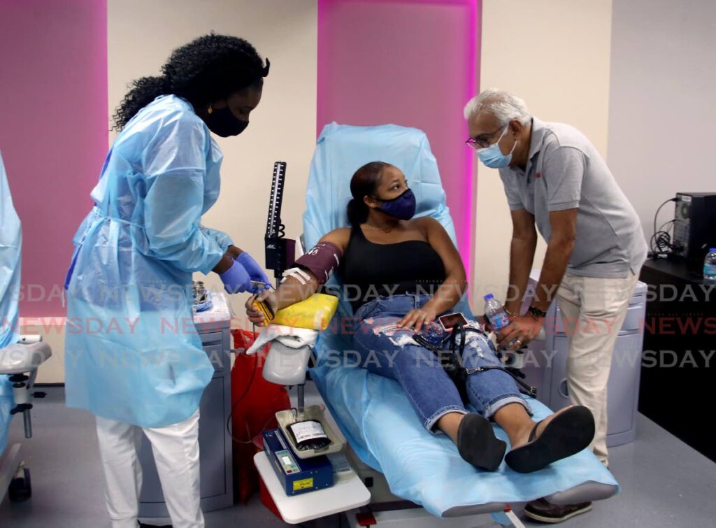 Health Minister Terrence Deyalsingh, right, speaks to first-time blood donor Onyca George at Eric Williams Medical Sciences Complex, on Saturday as a nurse prepares her for the procedure. - SUREASH CHOLAI