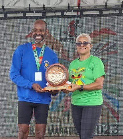 St Lucian Jason Sayers, left, collects his trophy from TT Olympic Committee president Diane Henderson after winning the TT Marathon at the Queen's Park Savannah, Port of Spain on Sunday. - 
