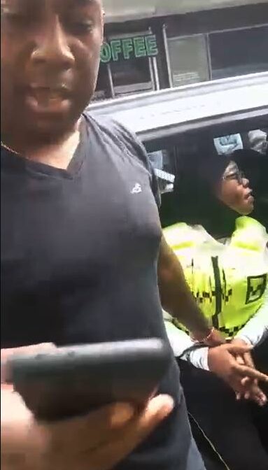 CALL: In this screen-grab of a video posted to social media, an off-duty policeman makes a call on his cell phone while holding on to a handcuffed traffic warden who sits in the officer's SUV on Frederick Street in Port of Spain on Monday. 