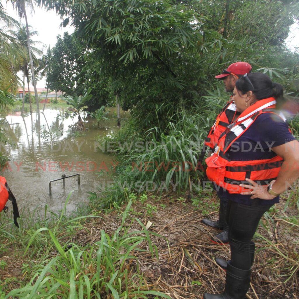 Disaster volunteers Rupa Amrit, Edwin Chin Hing and Sadia Ali-Sampath, observe as water from the Caroni River, filters freely into a pond at Bamboo # 2 on Monday because of a faulty flood flap. File photo/Angelo Marcelle