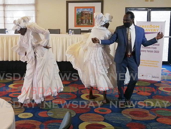 HAVING A GOOD TIME: National Security Minister Fitzgerald Hinds dances with sisters Stasha and Stashelle George of the Malick Folk Performing Company at the opening of the three-day forum on human trafficking at the Trinidad Hilton on Mnday. PHOTO BY JENSEN LA VENDE - 