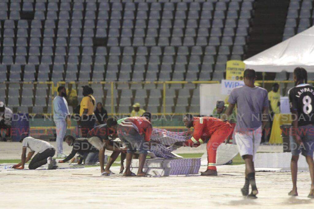 Workmen place a protective covering on the field of the Hasely Crawford Stadium around 9 pm on Friday ahead of the Machel Montano concert.