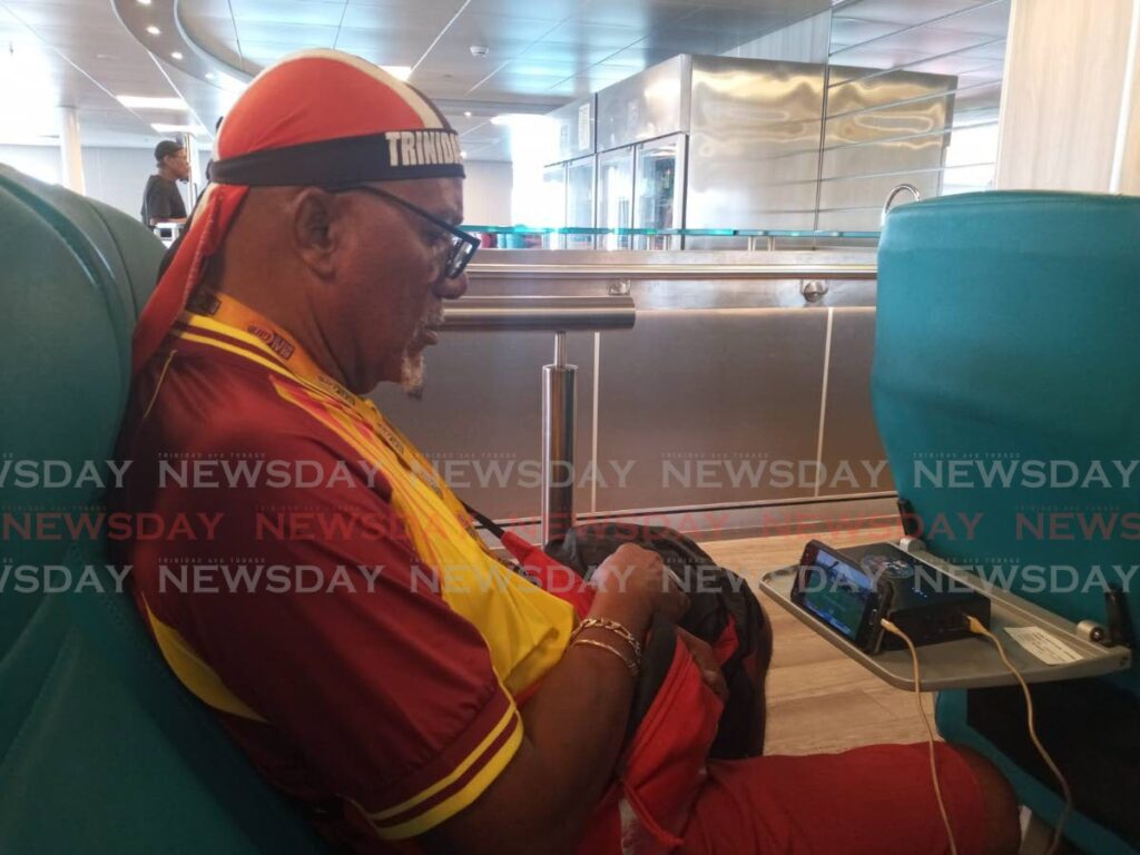 Joey Richardson, also knowns as Flagman, watches a West Indies game while on the Buccoo Reef fast ferry on Sunday, on the way to Tobago for a national football match. - Jelani Beckles