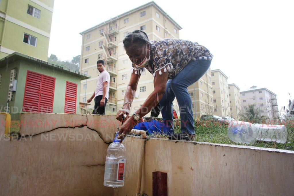 Julianna Charles a resident of Olera Heights HDC development, San Fernando stands in the rain to fill bottles of water as residents are complaing that the pumps have broken down and they are not getting a supply of water to the upper floors.