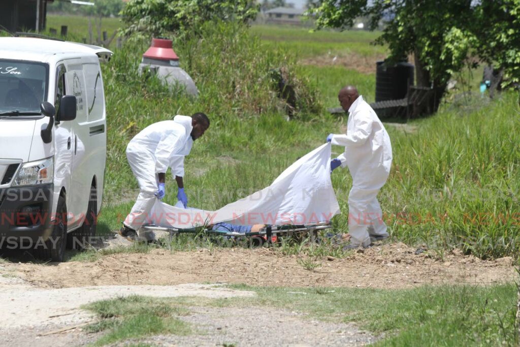 Undertakers remove the body of a man identified as Ronnie who was killed behind the Munroe Road Hindu Primary School, Cunupia on Monday. Photo by Angelo Marcelle