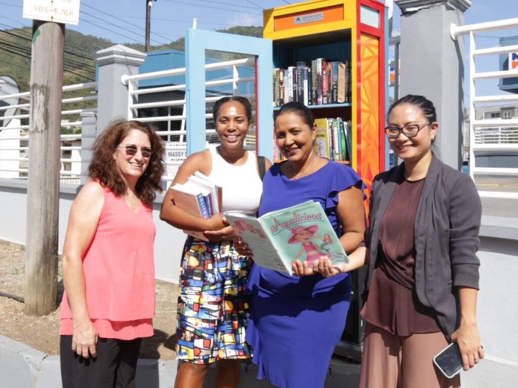 Maple Leaf International School teacher Cathy Sanders, from left, Cindy Allman of Book of Cinz, bmobile’s Anjanie Ramesar-Soom and another teacher of the school, Christal Fakoory, at the repurposed bmobile telephone booth which is now a Little Free Library located outside the school in Petit Valley.  - Photo courtesy bmobile