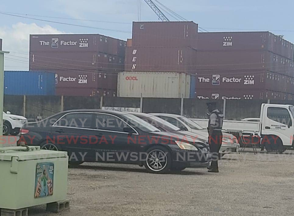 A police officer stands near a black Hyundai Elantra which was shot at by gunmen in the parking lot of Licensing Office on Wrightson Road, Port of Spain.  - Photo by Shane Superville
