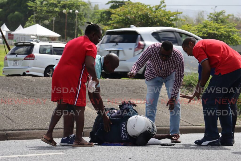 OFFICER DOWN: People attend to PC Alston Drakes after his motorcycle collided with the back of a stationwagon during midmorning rush hour traffic on the westbound section of the Churchill Roosevelt Highway near the Golden Grove Prisons on Friday. PHOTO BY ROGER JACOB  