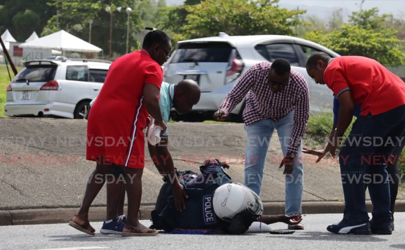 OFFICER DOWN: People attend to PC Alston Drakes after his motorcycle collided with the back of a stationwagon during midmorning rush hour traffic on the westbound section of the Churchill Roosevelt Highway near the Golden Grove Prisons on Friday.