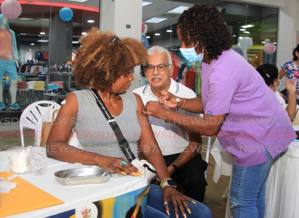 Health Minister looks on as a nurse gives a customer a vaccine during a health fair at Trincity Mall in April. - AYANNA KINSALE