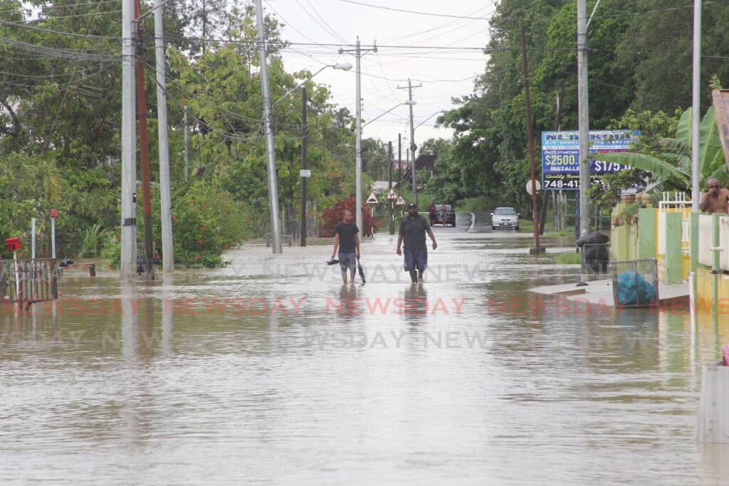 Two men walk through a flooded Suchit Trace, Debe, on Monday. - Lincoln Holder