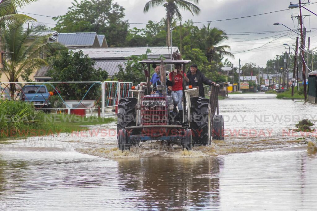RESCUE TEAM: Barrackpore residents including Haffize Mohammed and Nick Boodram use a tractor to drive through floodwaters on New Colonial Road, in an effort to find and help stranded residents on Monday. - Lincoln Holder